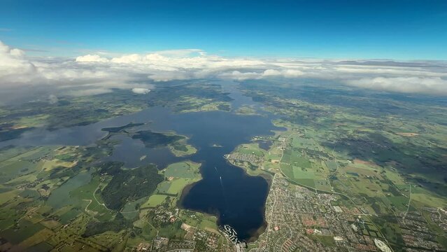 Airplane side view descent landing Copenhagen with grassland and lakes and solid cloud cover rolling in with mist or fog arch