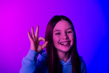 Photo of cheerful pretty little lady dressed hoodie showing okey gesture empty space isolated neon purple color background