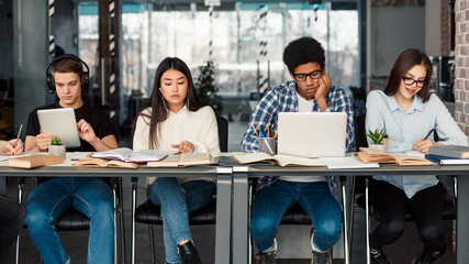 Students using different gadgets studying in university library and preparing for exams