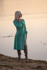 Portrait of a young beautiful blonde girl in a dress by the river.