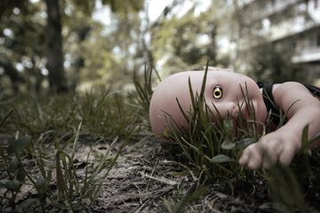 Creepy doll with scary yellow eye lies on the ground. A scary plastic doll lies in the grass with...