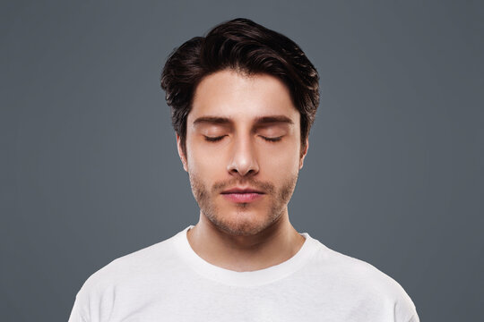 Portrait of handsome millennial man with closed eyes, grey studio background