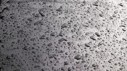 This image captures raindrops on a dark surface, highlighting their glistening clarity and natural beauty.