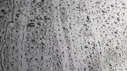 This image captures raindrops on a dark surface, highlighting their glistening clarity and natural beauty.