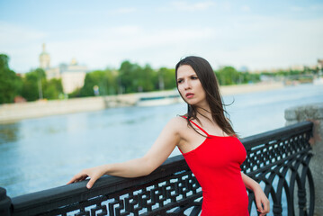 A woman in a red dress stands on a pier overlooking a body of water. She is looking off into the distance with a pensive expression on her face. Concept of solitude and contemplation