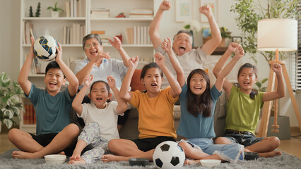Cheerful multi-generation asian family having fun while watching a game of their favorite sports...