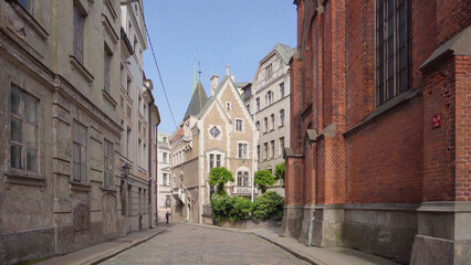 Street in the center of riga, it is cobblestone and the old buildings offer a picturesque view, one of the buildings is old and unmaintained and the other is red brick.