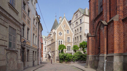 Obraz premium Street in the center of riga, it is cobblestone and the old buildings offer a picturesque view, one of the buildings is old and unmaintained and the other is red brick.