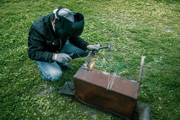 A welder in a protective mask constructs industrial steel. Industrial steel welder or outdoor equipment repair