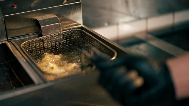 close-up in a professional kitchen frying chicken wings in oil in a deep fryer chef hold
