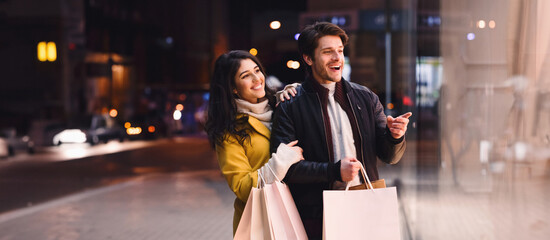 A man and woman are seen casually strolling down the street while holding shopping bags in their...