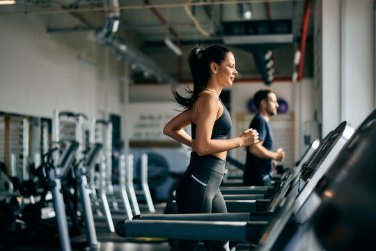 Side profile of a female running on a treadmill at the gym, a male running in the background.