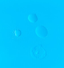 Refreshing droplets and dabs of hydrating clear skincare gel set against bright blue background,...