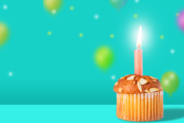 Birthday cupcake with lit candle on green background with colorful balloons. Copy space