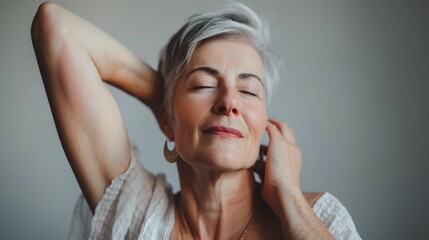 Obraz premium A woman with short gray hair closed eyes and a serene expression gently resting her chin on her hand wearing a white blouse and a gold necklace.