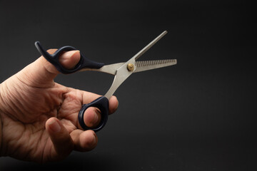 a man's hand is holding a hair scissors that used for the hair thinning process