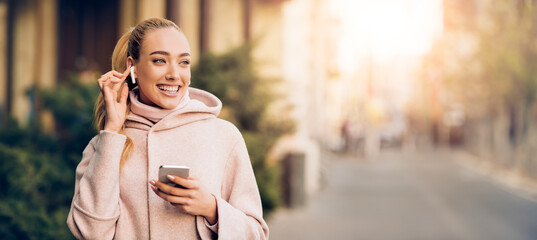 Happy girl enjoying music in airpods, walking in city center at autumn day