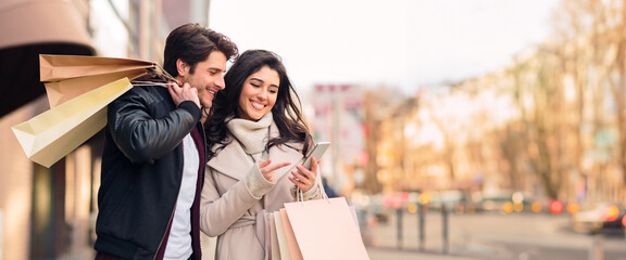 A couple holding shopping bags while looking at their phone together outdoors.
