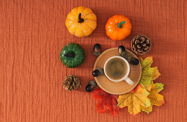 Colorful autumn or fall scene made with autumn leaves, nuts and cup of coffee on brown muslin background. Minimal seasonal concept. Nature flat lay composition.