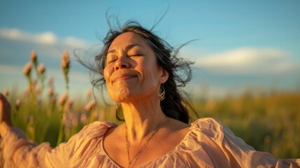 Obraz premium A woman in a pink blouse with her eyes closed smiling and enjoying the breeze in a field of flowers.