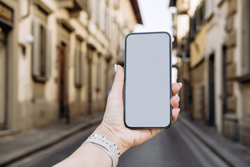 Blank screen smartphone , smartphone in a woman's hand on the background of a European street, mockup for an app for hotel booking and apartment rental and delivering