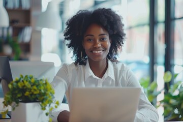 Successful Afro businesswoman smiling at laptop in modern office.