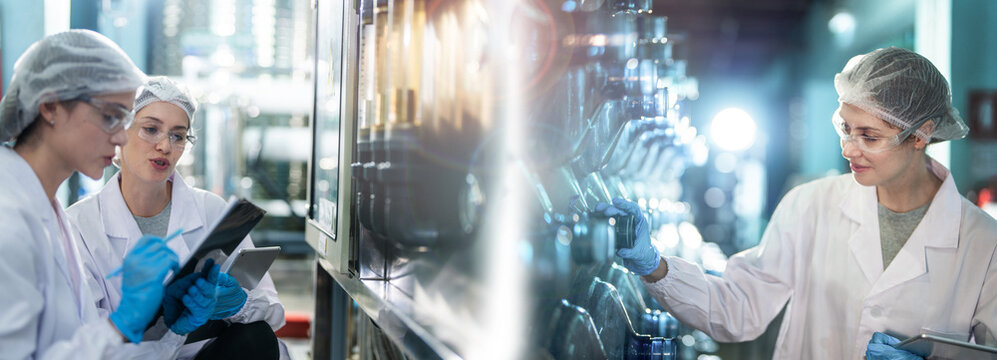 Female factory workers check machine systems at the industrial factory. Women working in clean rooms for beverage and food production