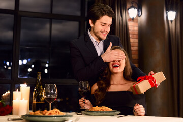 Happy handsome man giving a surprise Valentine's day present to his excited girlfriend, have date at restaurant. Valentine Gift concept