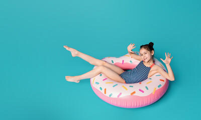 A young girl is lying comfortably on a brightly colored inflatable donut in a sunny outdoor setting. She looks relaxed and content as she enjoys floating on the water.