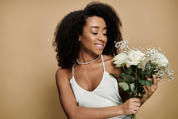 African American woman with natural makeup holds white roses and smiles softly, looking down at the flowers.