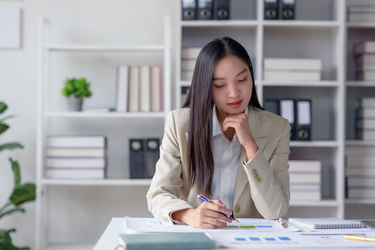 Focused businesswoman analyzing documents in modern office, contemplating data and strategies for company growth.