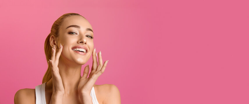 Portrait of beautiful woman touching skin or applying cream over pink background