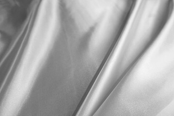 Gray fabric texture background. Close-up shiny satin fabric texture with copy space. Concept of simplicity, silver, luxury, fashion, cloth, and textiles. Soft black-grey background of wavy satin.