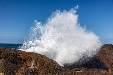 Wave breaking on rock in Point Lobos Nature Preserve, Monterey, California. Spray in the air. Blue sky, Pacific ocean in the background. 
