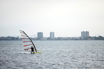 Unrecognizable windsurfer surfing in the Mediterranean sea with a skyline landscape.