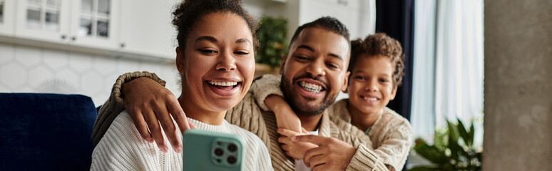 Man and woman smiling, taking selfie with cell phone, with son.
