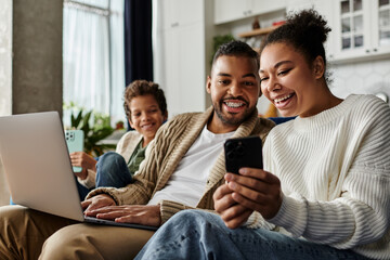 Man and woman engrossed in cell phone while seated on couch, with son.