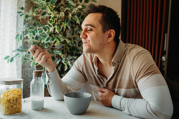 One young caucasian man is eating corn flex breakfast at home before work	