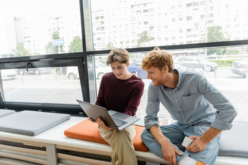 Two male students focused on a laptop while sitting on a bench.