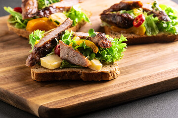 Tasty homemade sndwiches with grilled vegetables and sausages and fresh juicy salad leaves on the serving board close up.