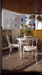 Cozy outdoor patio with white metal chairs and a round table, decorated with potted plants and wooden ceiling, creating a serene and inviting atmosphere perfect for relaxation or outdoor dining