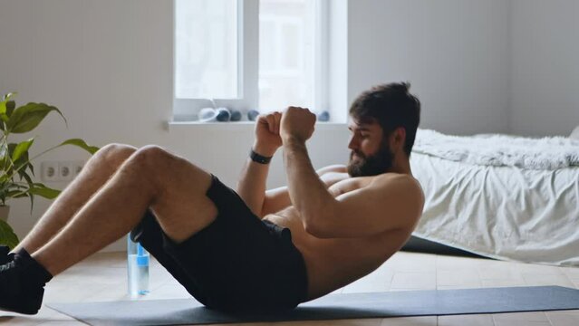 Young man doing abdominal exercise, practicing crunches at home on floor