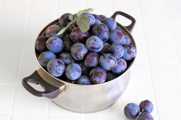 Ripe blue plum in an iron pan on a white table. Harvesting fruits and berries, preservation