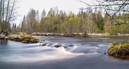 A fascinating panoramic long-exposure shot of the Kapsha River with rapids made of stones in May with snow lying on the other bank