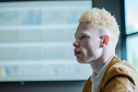 Confident young businessman with albinism listens attentively in a modern office meeting, showcasing diversity and leadership