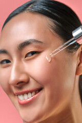 Acne treatment method. Smiling asian female dropping transparent serum from pipette on cheek and looking at camera. Confident human using professional cosmetic after dermatology consultation.