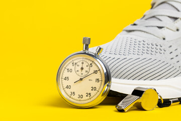 Sports shoes, whistle and stopwatch on yellow background. Sports equipment.