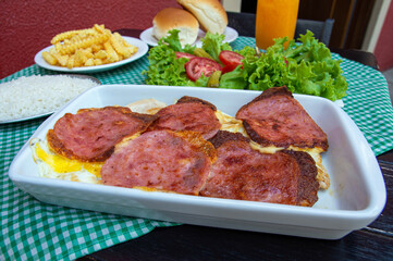 Restaurant table with steak that have cheese and ham on top, french fries, white rice, bread, salad and orange juice. In Brazil, all these we call a complete bauru. Typical brazilian food.