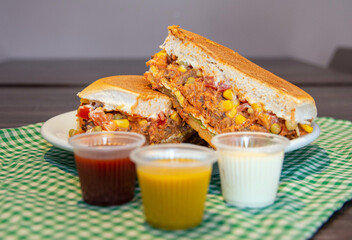 Delicious fresh beef strogonoff burger cut in half, with bread, beef, cheese, tomatoes, lettuce, egg, corns, peas and sauce. This type os food is known as xis in Brazil.
