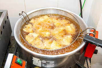 Fried fish being prepared in professional restaurant kitchen. The chef puts delicious fish in the fryer.The oil boils.